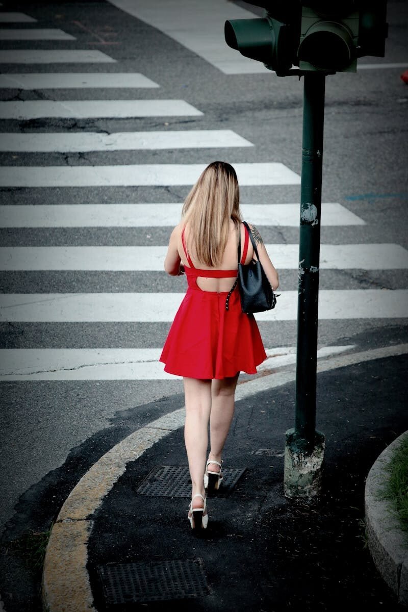Back view of a woman in a red dress crossing a city street at a pedestrian crossing.