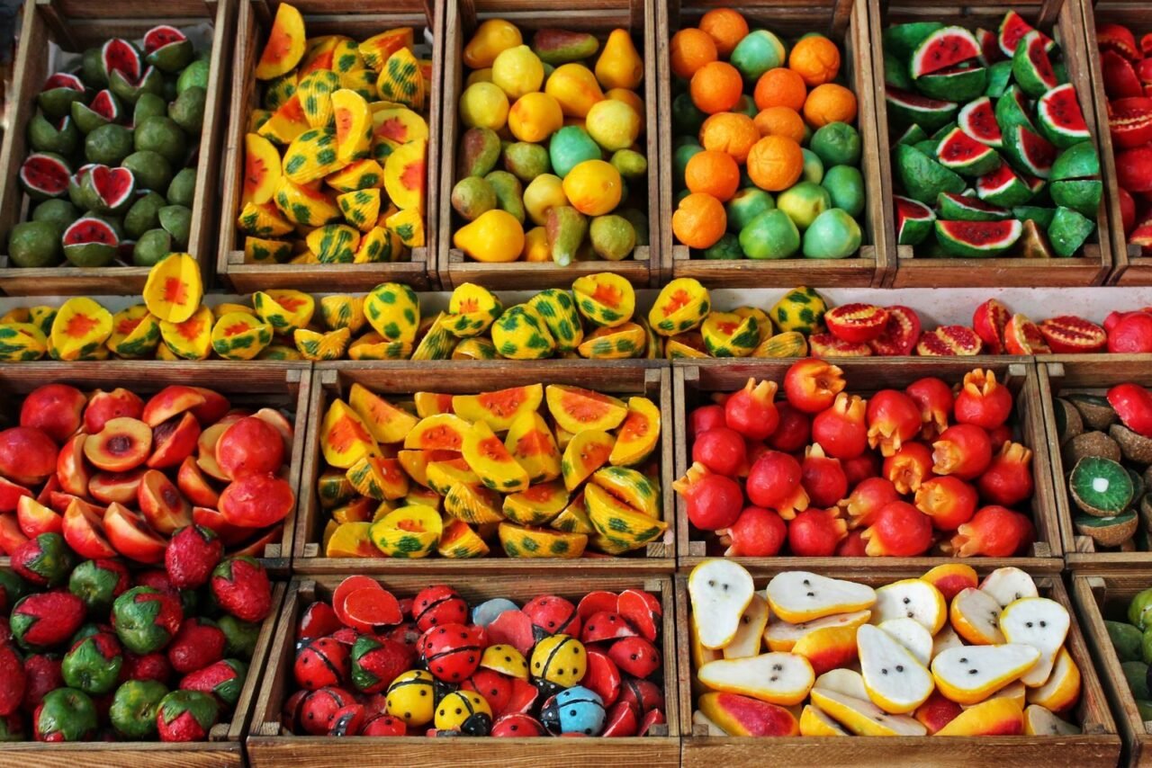 Colorful assortment of fruit-shaped handmade soaps displayed in wooden boxes.