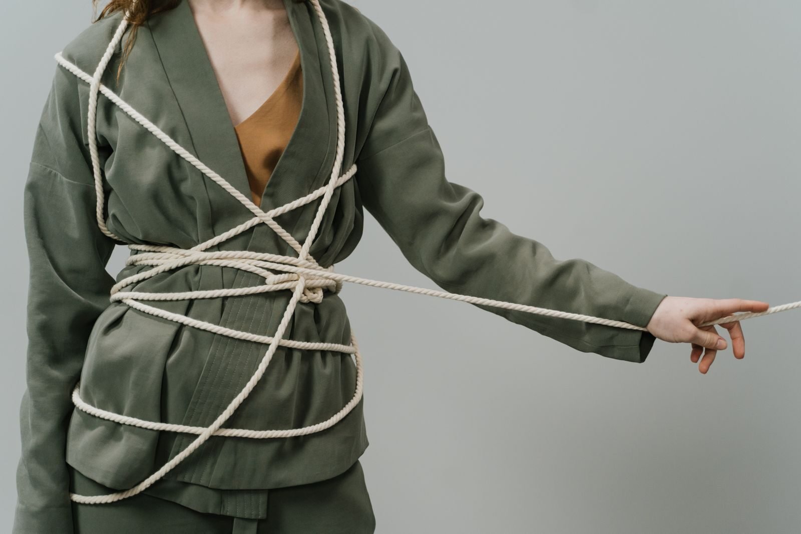 A woman in green attire artistically bound with rope on a gray background.