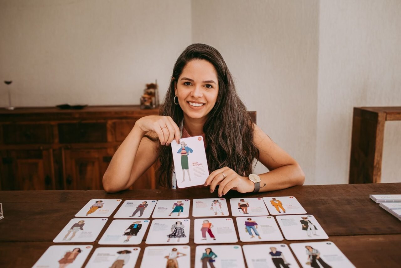 Smiling woman with fashion cards on table, showcasing outfits and styles indoors.