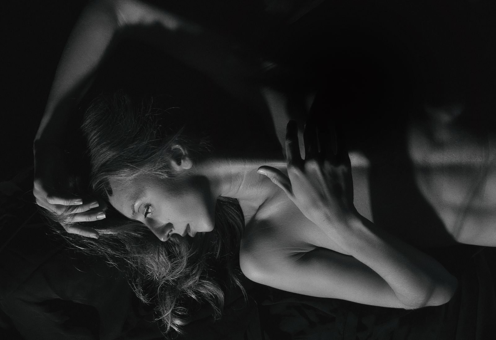 A dramatic grayscale portrait of a woman lying down, featuring high contrast lighting.