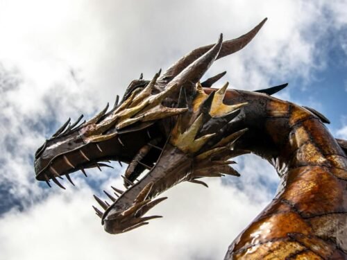 A striking low-angle view of a dragon statue set against a cloudy sky.