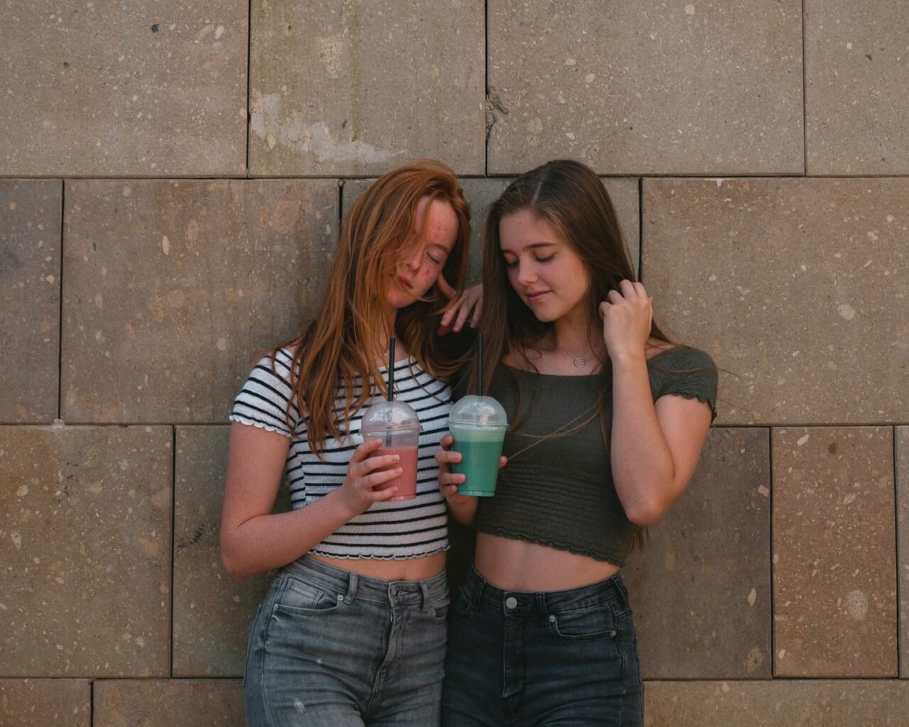 two women leaning on gray wall