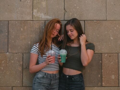 two women leaning on gray wall