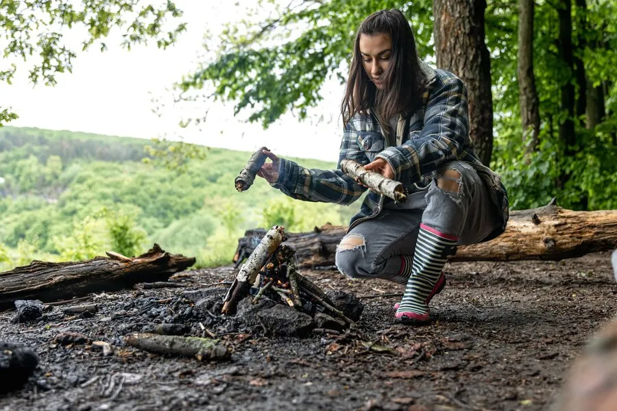 Attractive young woman makes fire keep warm forest