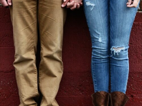 Couple holding hands, standing in front of a wall.