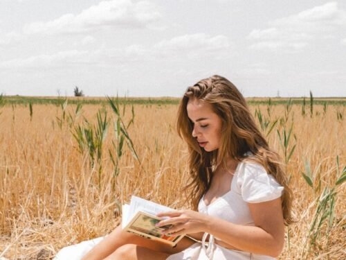 a woman sitting in a field reading a book