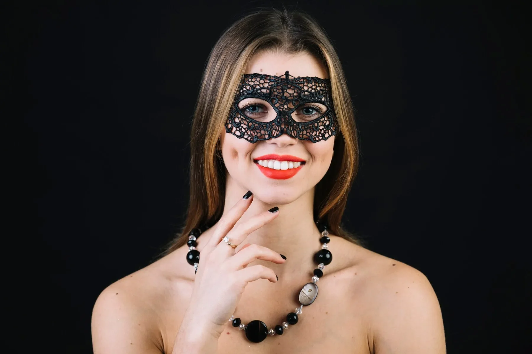 Cheerful woman wearing carnival mask necklace black background