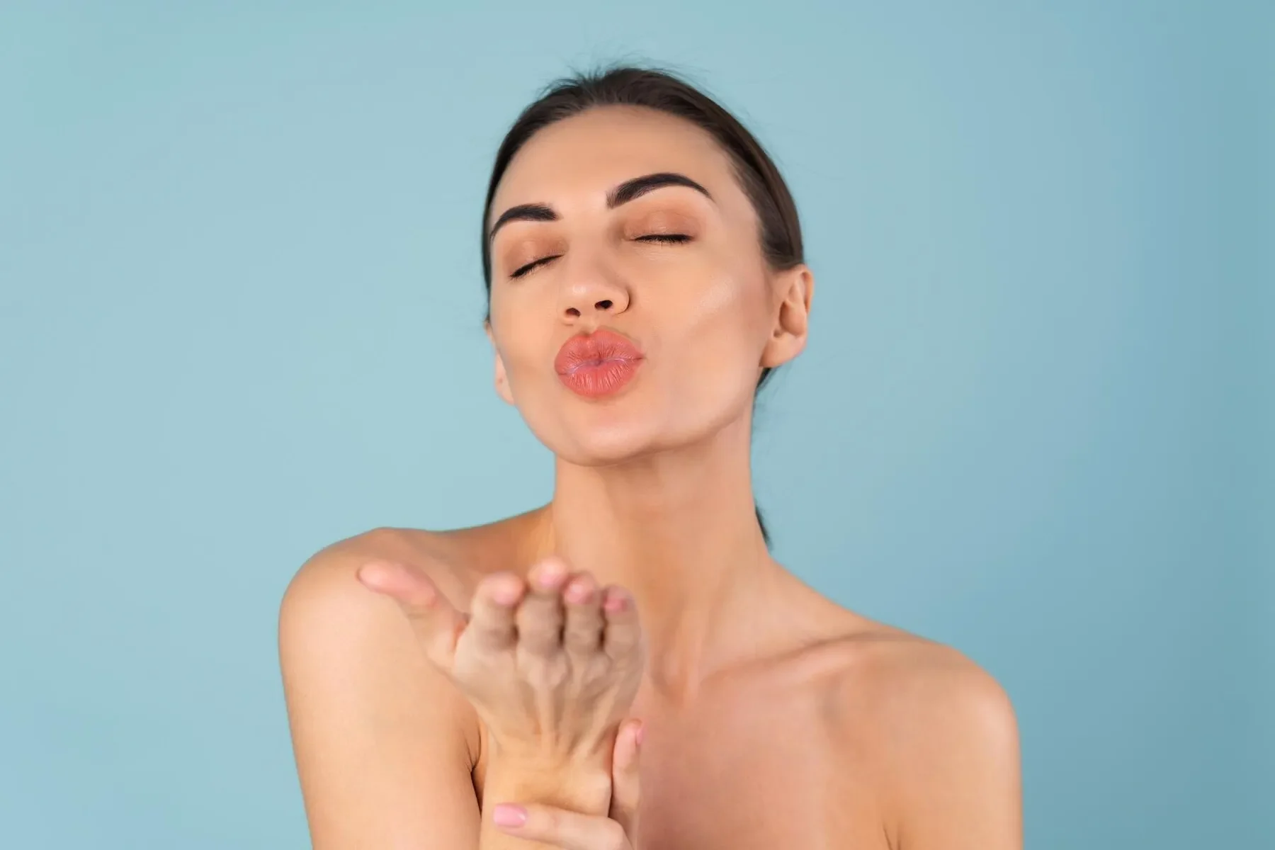 Close beauty portrait topless woman with perfect skin natural make up plump nude lips blue background sends kiss