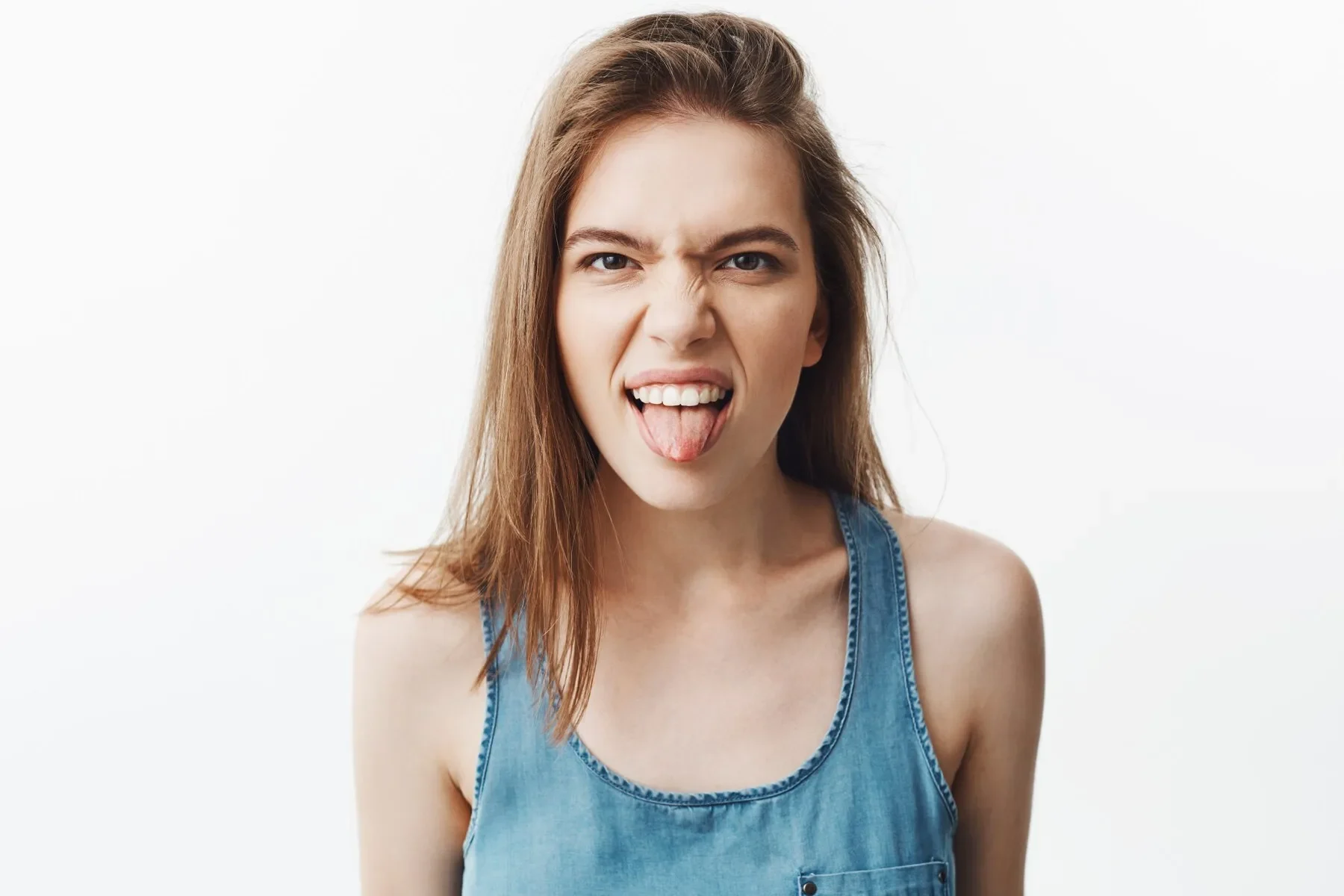 Close up silly good looking caucasian young woman with dark hair blue shirt showing tongue