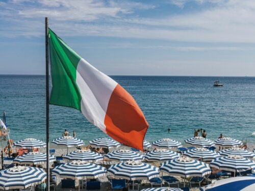 a large italian flag flying over a beach filled with umbrellas