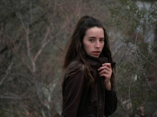 woman in brown leather jacket standing beside trees during daytime