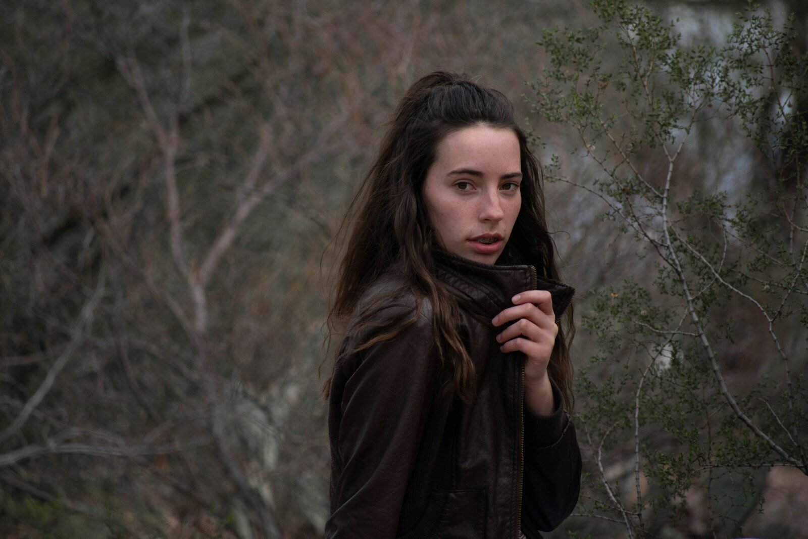 woman in brown leather jacket standing beside trees during daytime