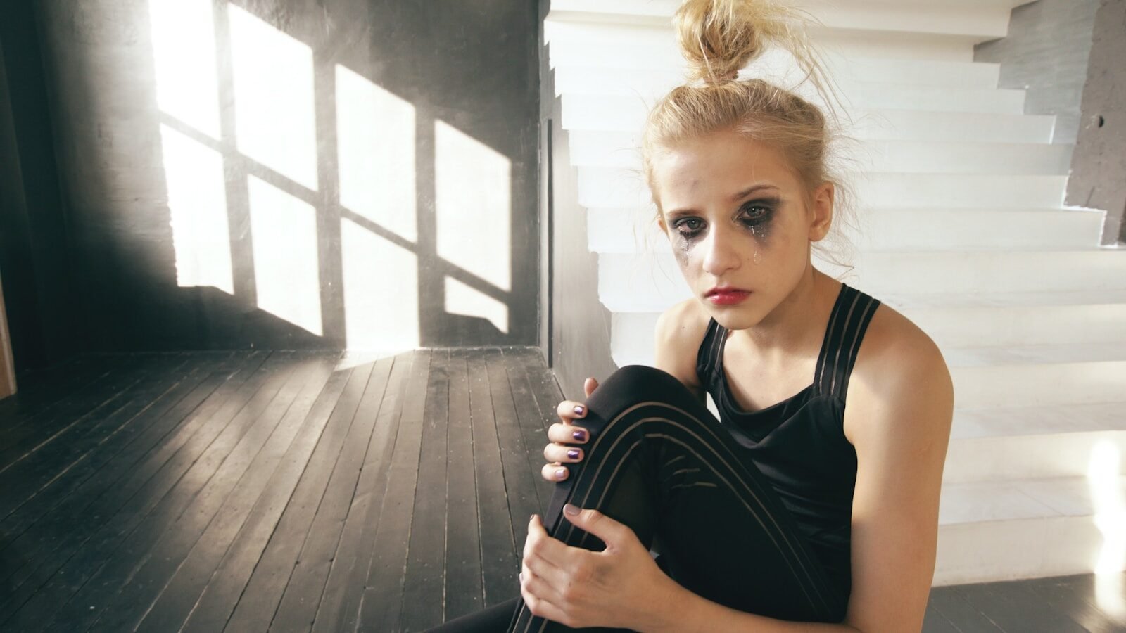 Sad young girl with smudged makeup sits on floor.