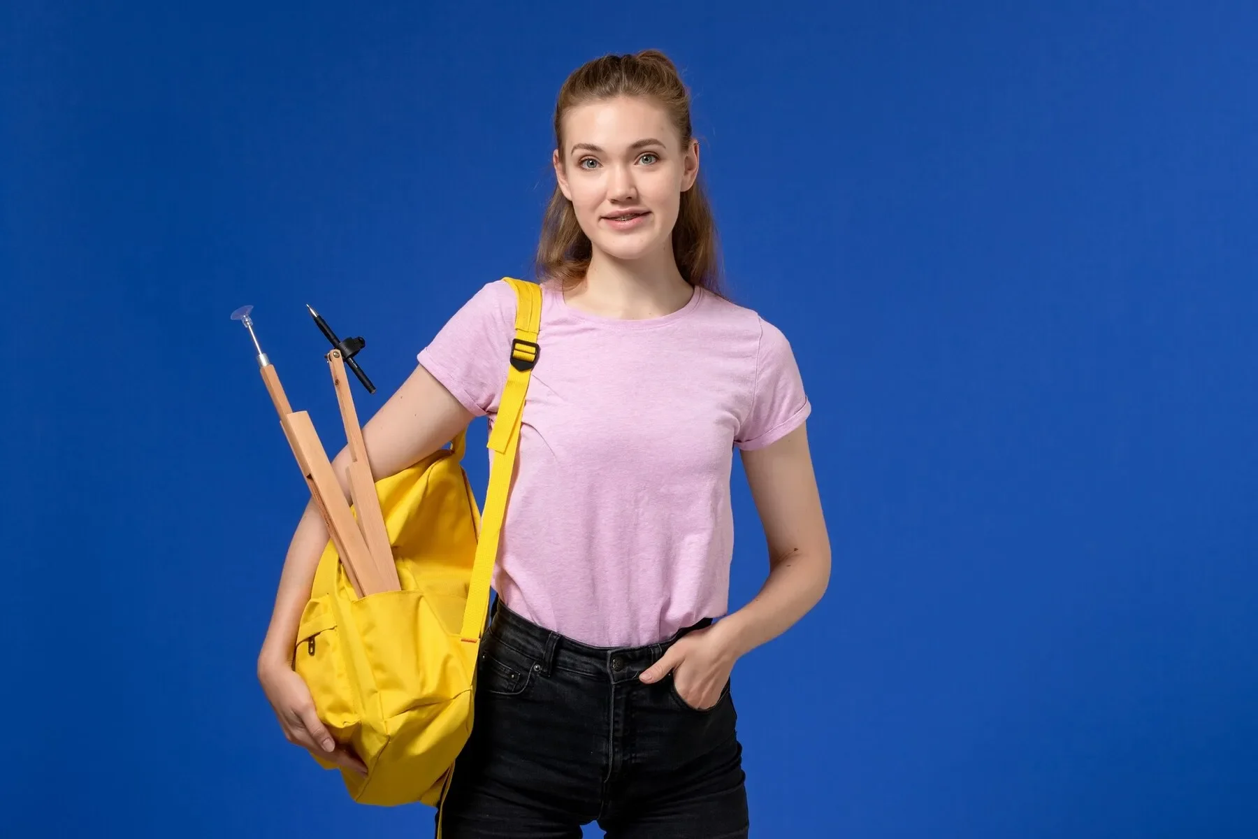 Front view young female pink t shirt wearing yellow backpack blue wall