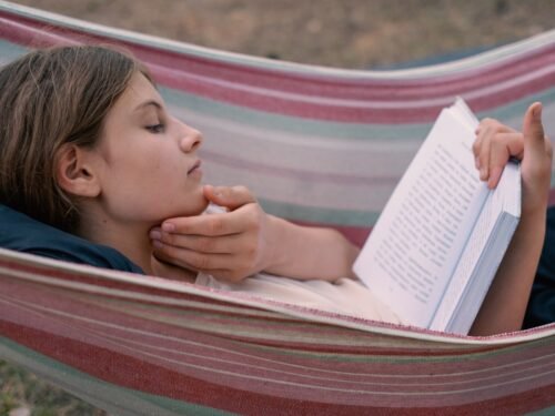 Young girl reading a book in a hammock.