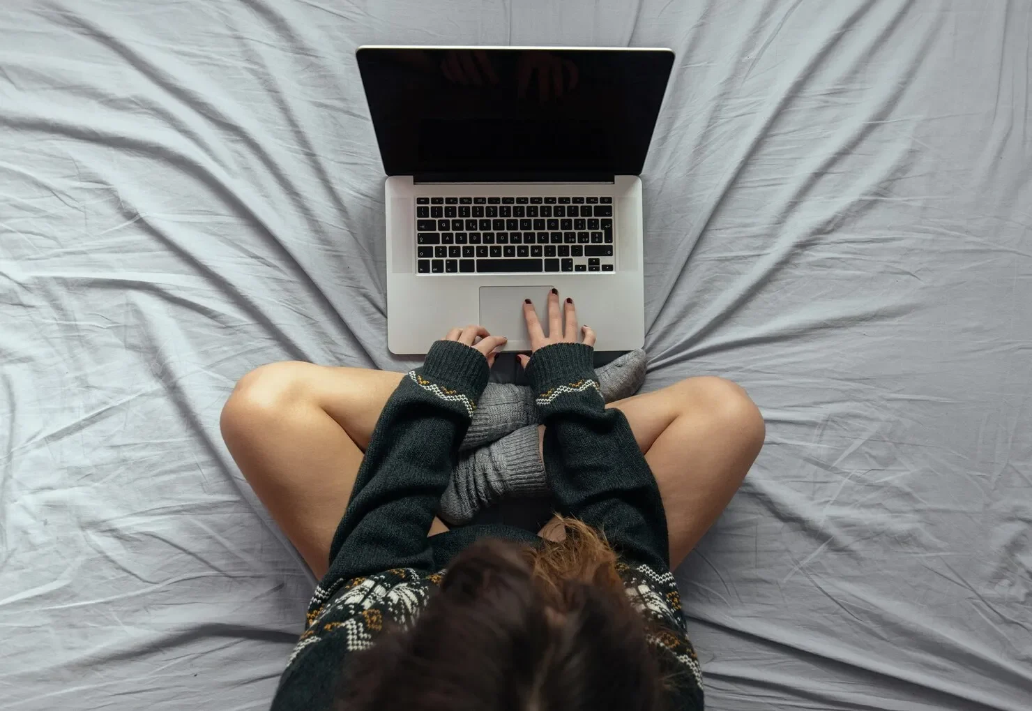High angle shot female typing laptop while sitting bed with crossed legs