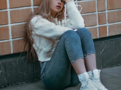 a woman sitting on the ground next to a brick wall
