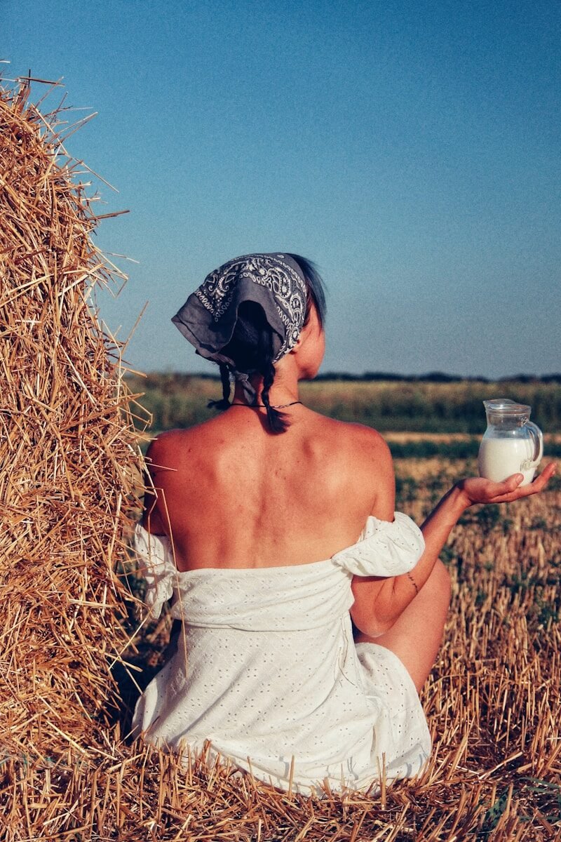 a woman sitting in a field holding a glass of milk