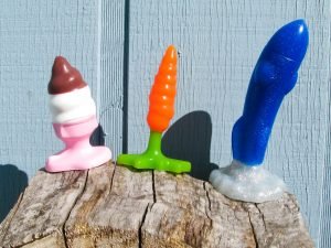 Hole Punch Toys Ass Cram Cone, Plugs Bunny, and Crotch Rocket standing on a wood pile in front of a pale blue house.