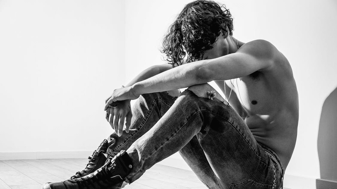 man with no shirt sitting against wall