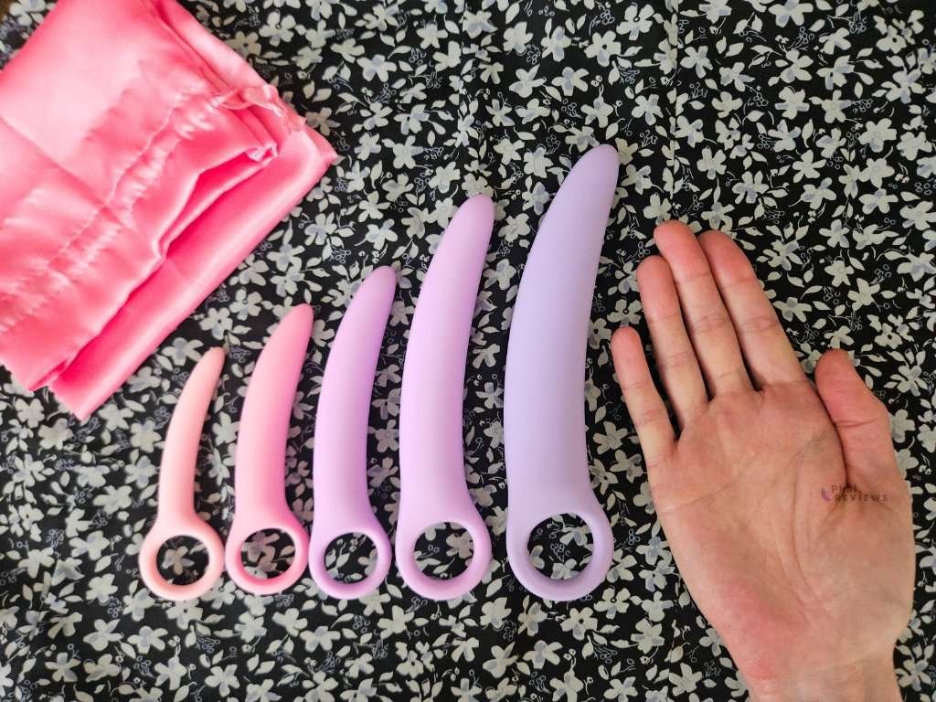 Five silicone vaginal dilators arranged from smallest to largest next to a hand for size comparison, showing gradual progression for comfortable dilation and stretching