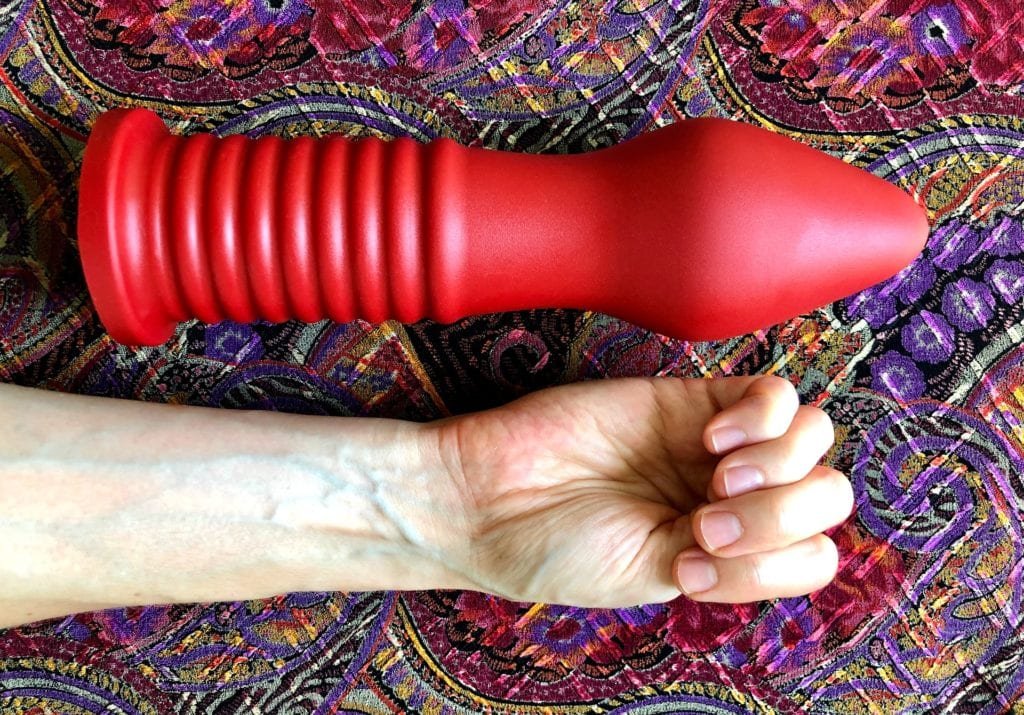 Large silicone fisting dildo shown next to a hand for size comparison