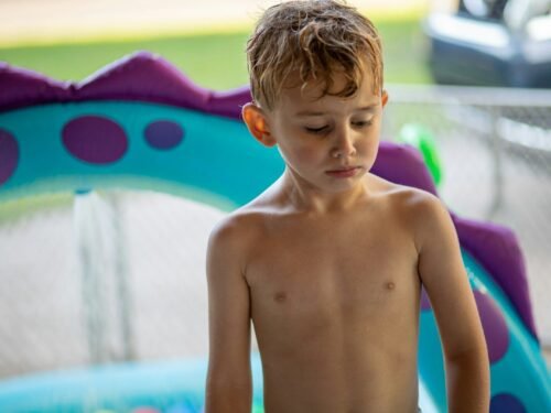 topless boy standing near swimming pool during daytime