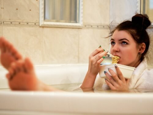 girl in bathtub holding white ceramic mug