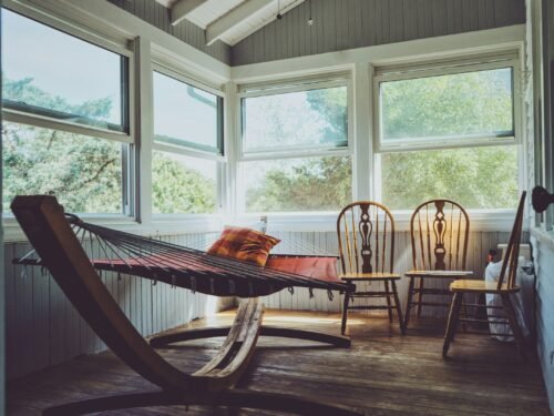 photography of grey, white, and brown wooden house interior with three brown wooden Windsor chairs beside brown hammock with glass windows