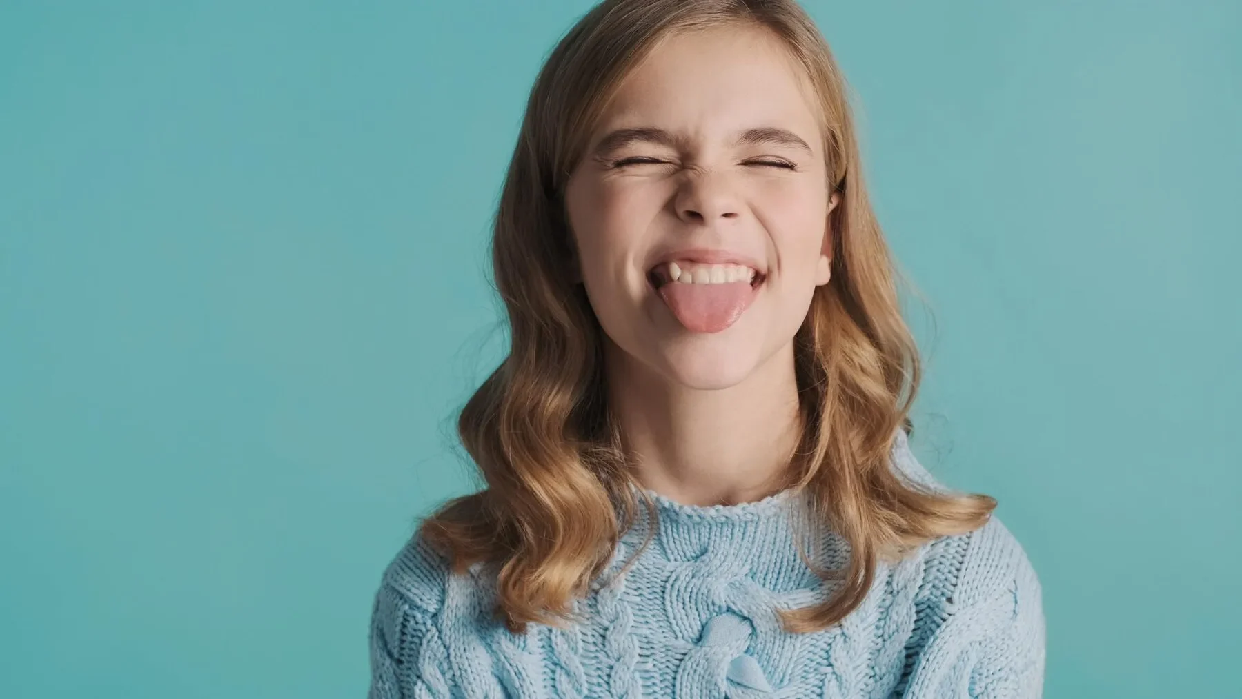 Pretty blond teenage girl with wavy hair showing tongue