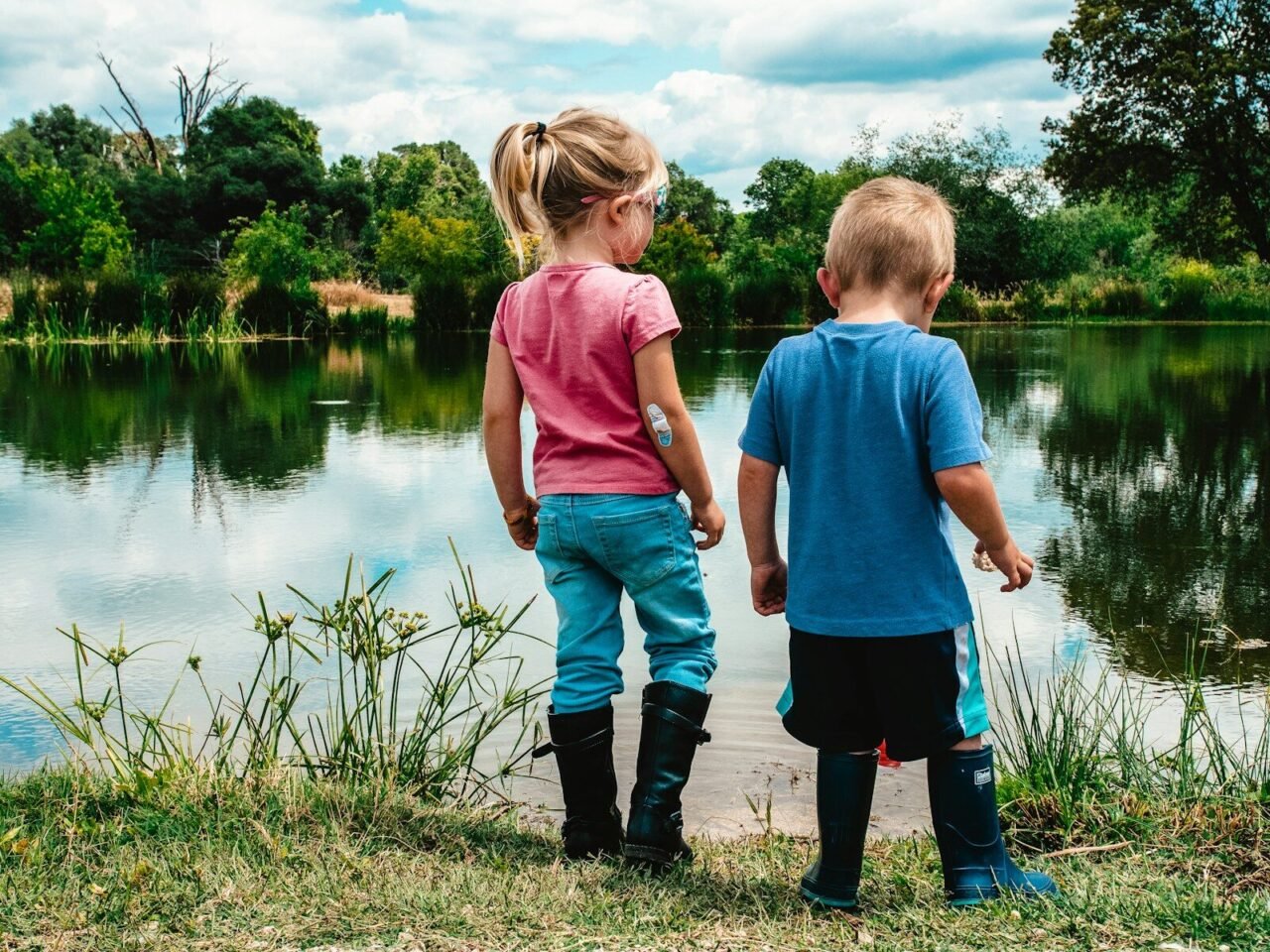 2 boys standing on green grass near lake during daytime