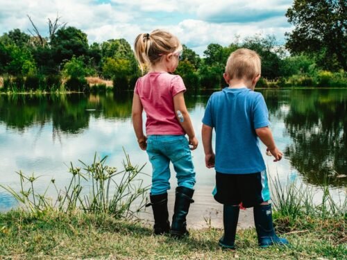 2 boys standing on green grass near lake during daytime