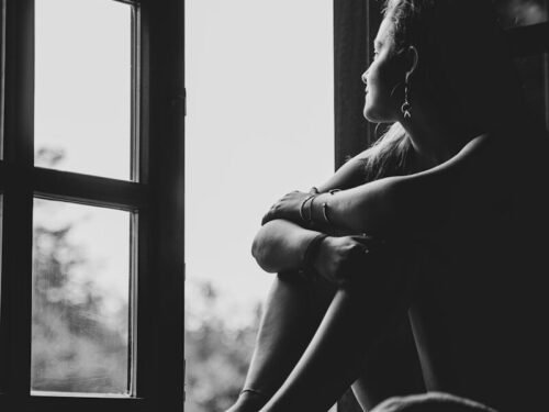 grayscale photo of woman sitting on window