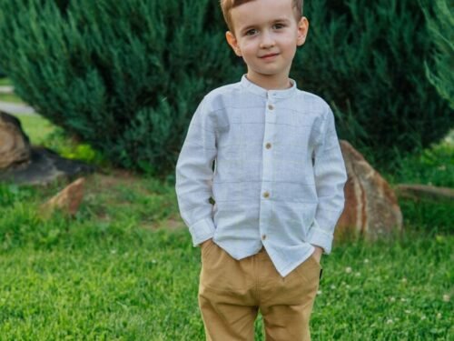 boy in blue dress shirt and brown pants standing on green grass field during daytime