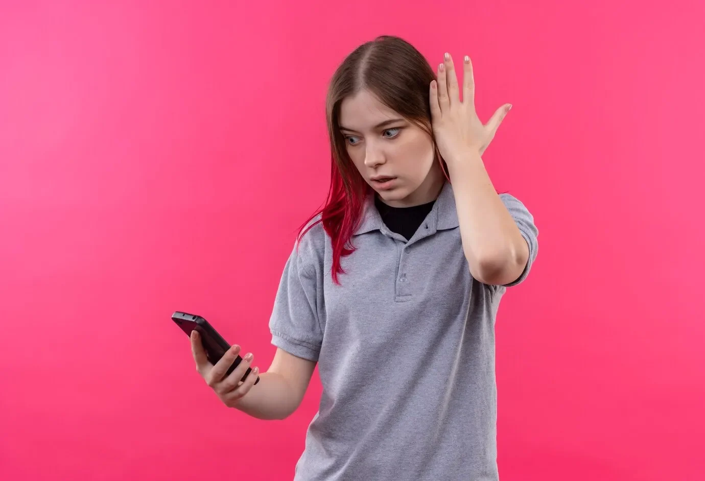 Surprised young beautiful girl wearing gray t shirt looking phone her hand