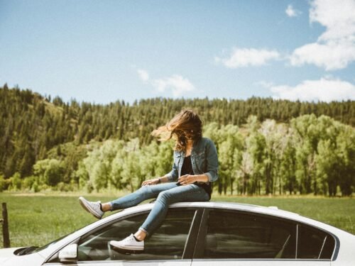 woman sitting on roof of white sedan