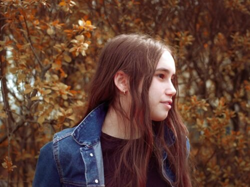 woman standing and facing her right side surrounded with tall and brown trees