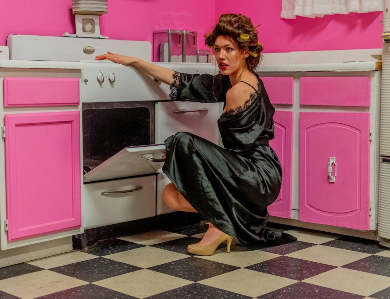 A woman in a black dress is opening a pink oven
