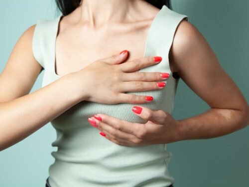 Woman performing breast self-examination against a teal background.