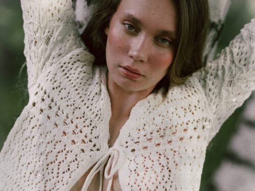 A person leans against a tree wearing a cardigan.