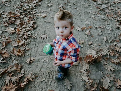boy in white, blue, and orange plaid button-up shirt holding green cup