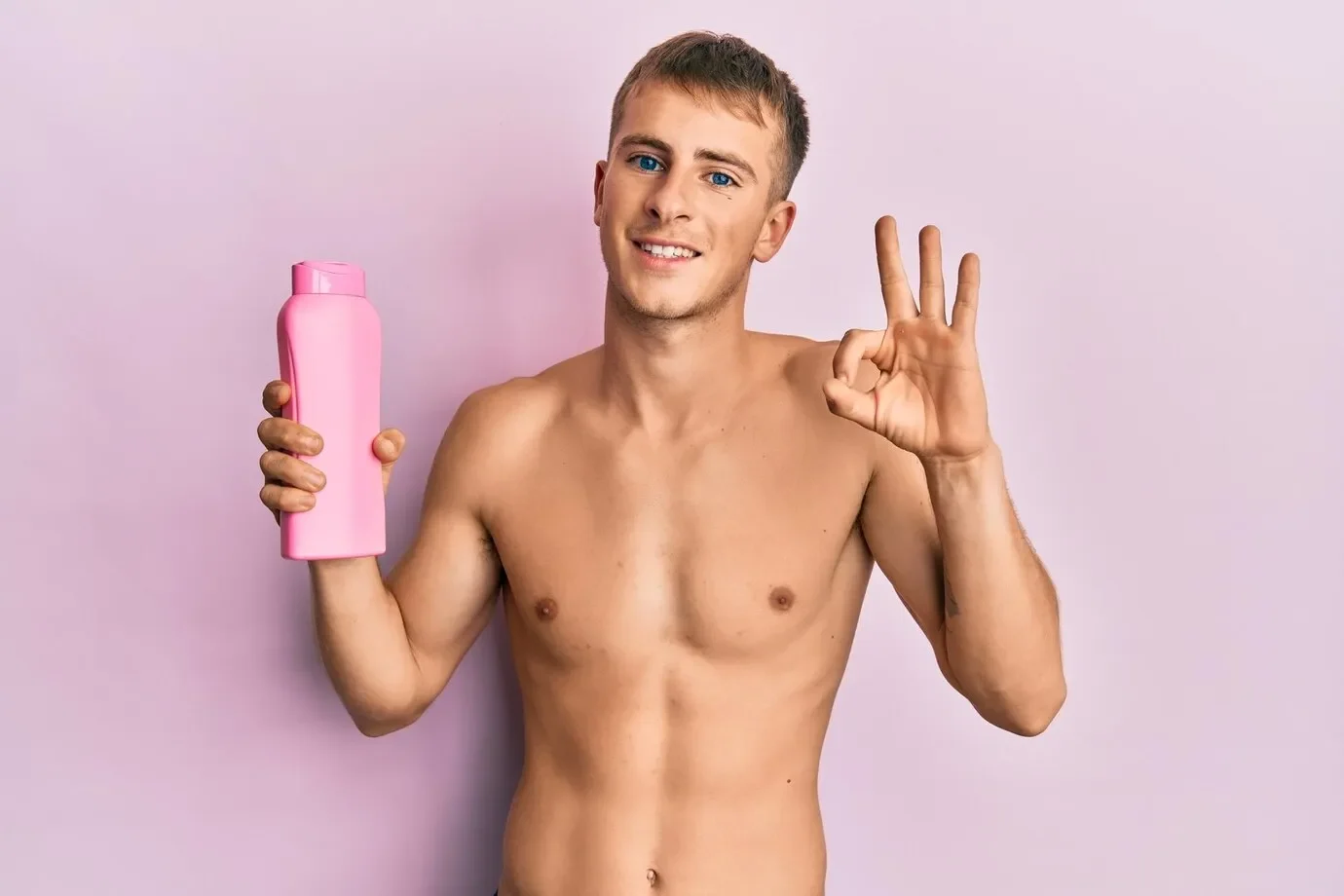 Young caucasian man shirtless holding shampoo