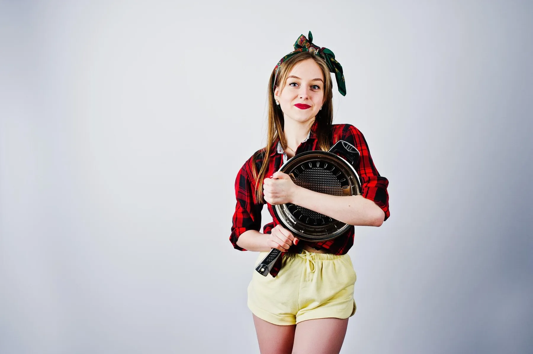 Young funny housewife checkered shirt yellow shorts pin up style with frying pan isolated white background