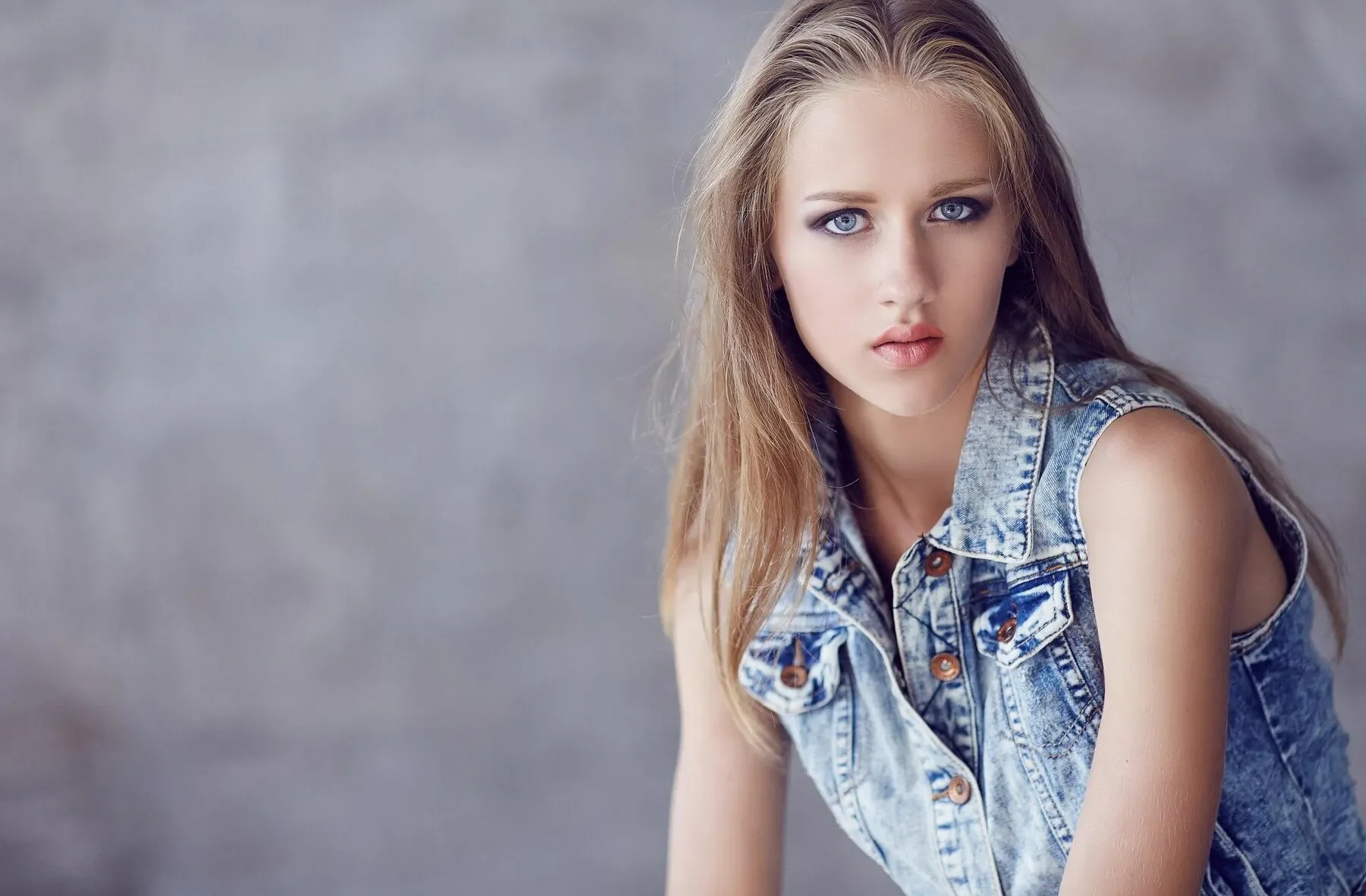Young woman denim jacket black pants posing near concrete wall